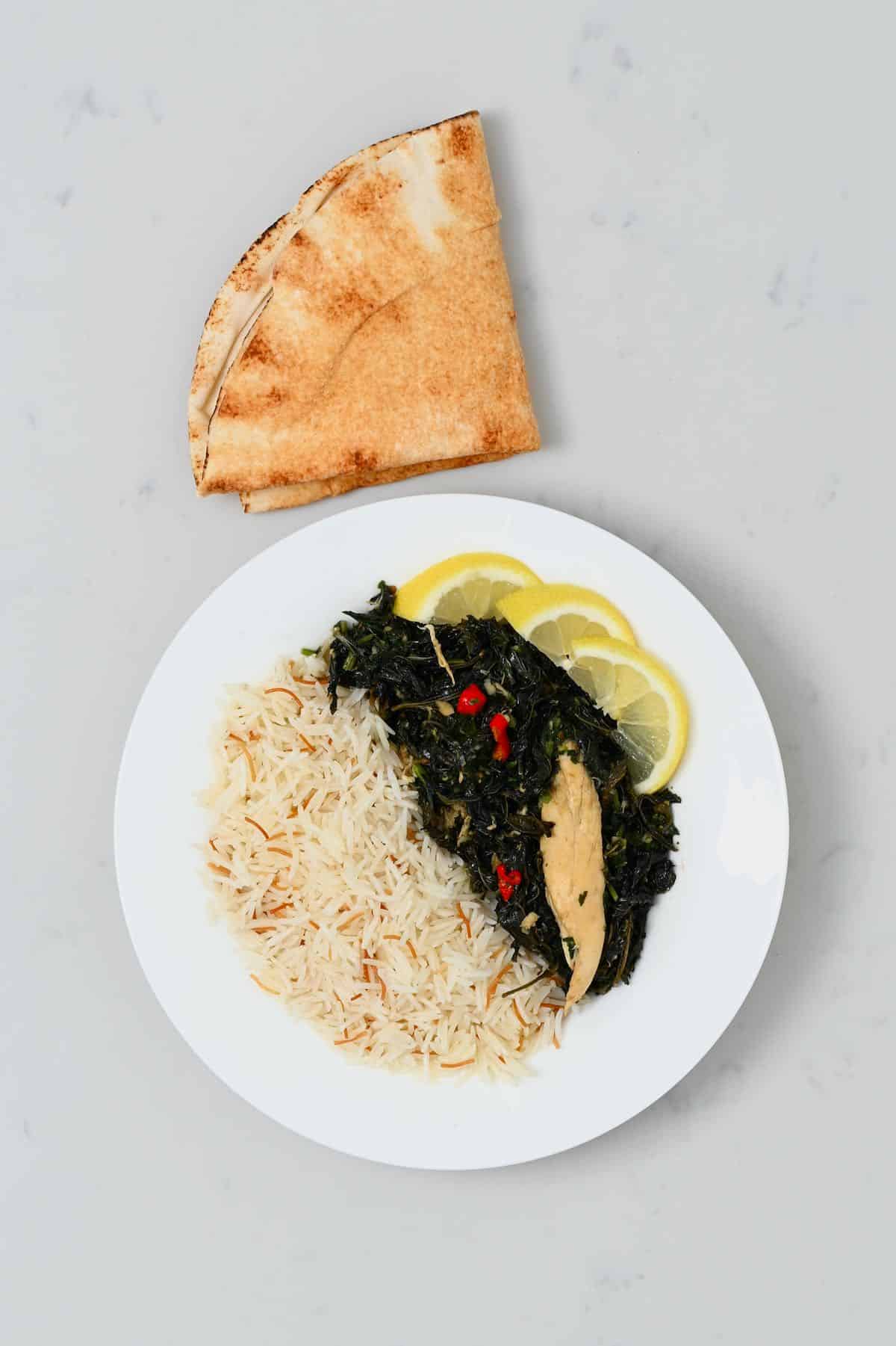 A serving of molokhia with chicken rice and pita