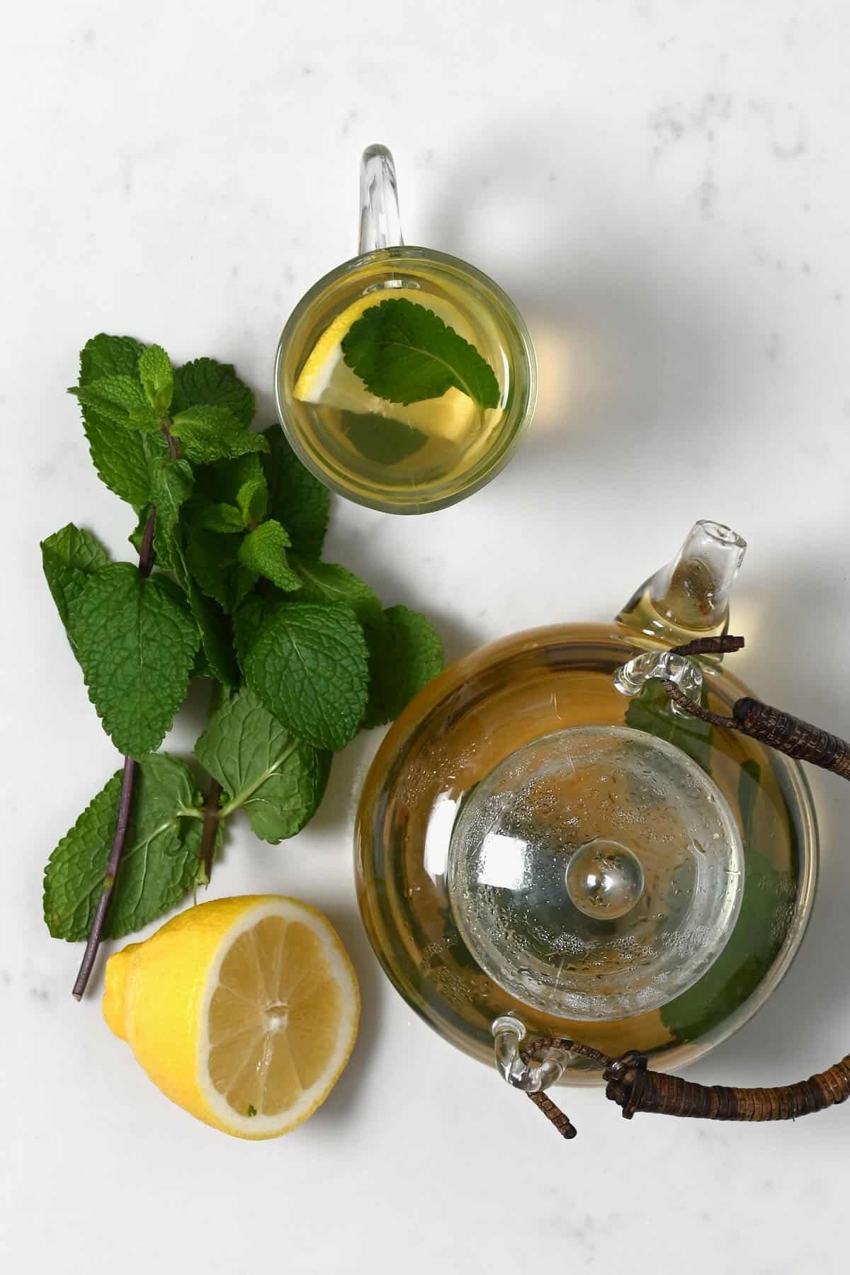 A glass and a teapot with mint tea and lemon slice