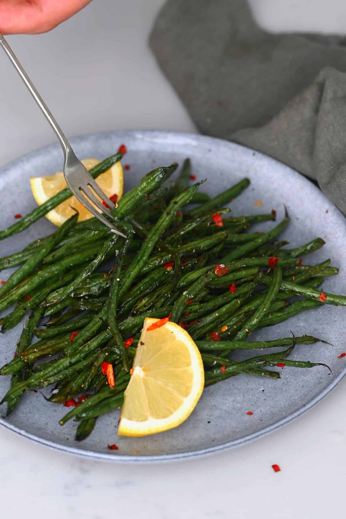A serving of air fried green beans with lemon wedges