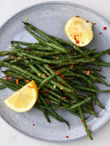A serving of air fried green beans with lemon wedges