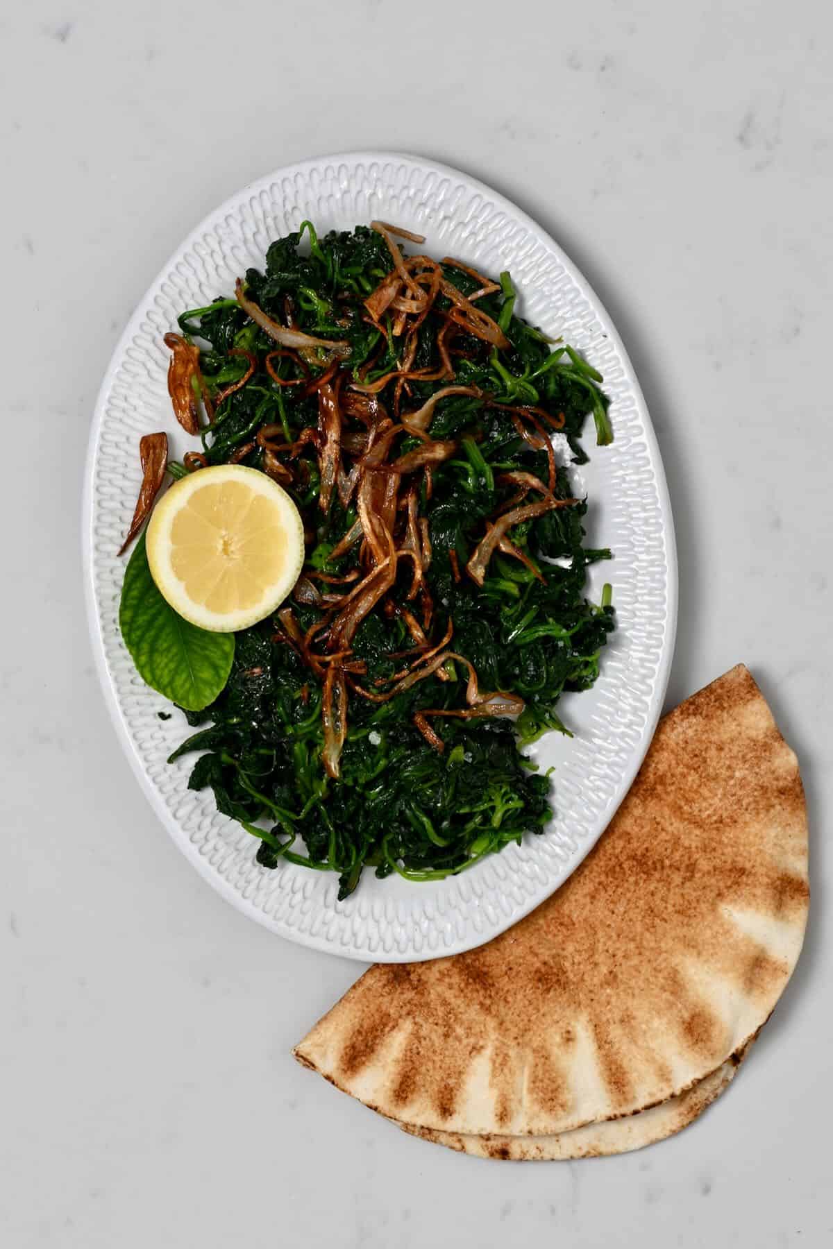 A plate with spinach and crispy onion and pita bread