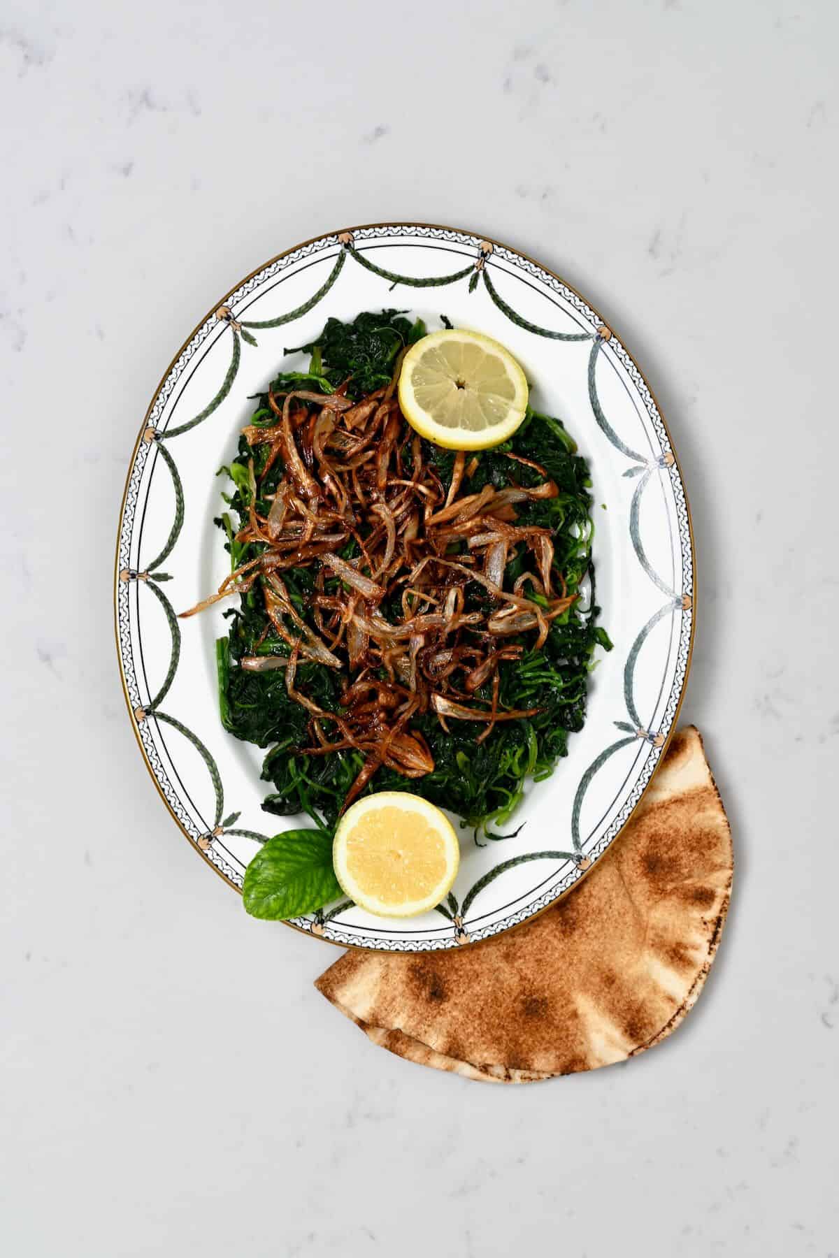 A serving plate with spinach and crispy onions and lemon