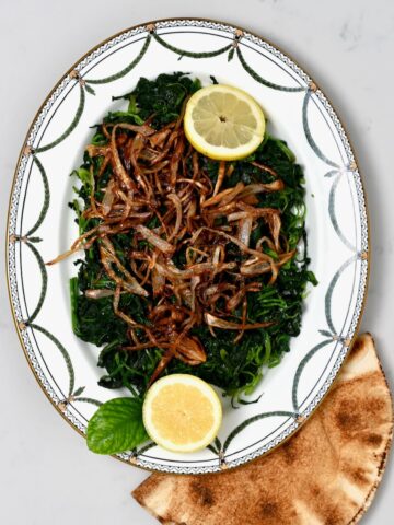 A serving plate with spinach and crispy onions and lemon