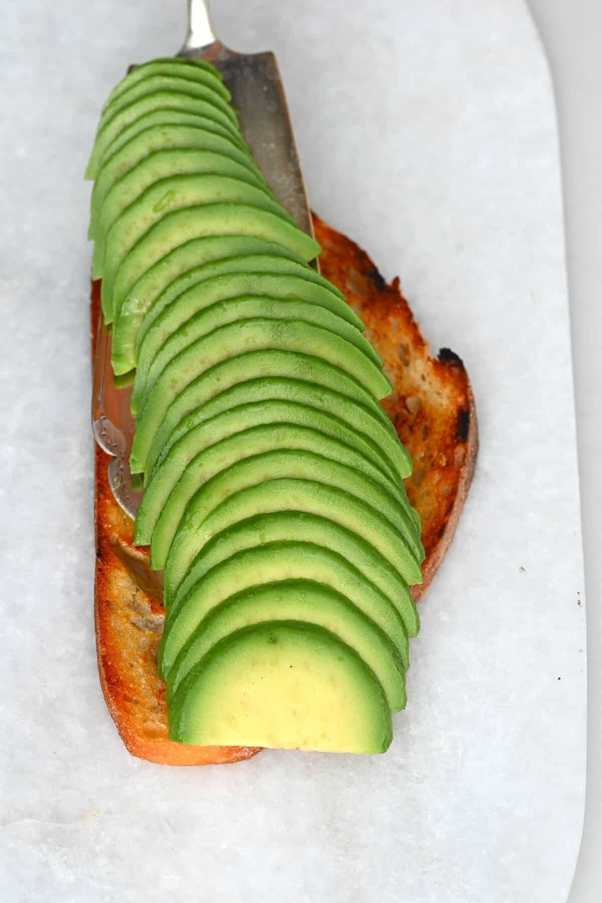 Placing avocado slices on slice of toasted bread