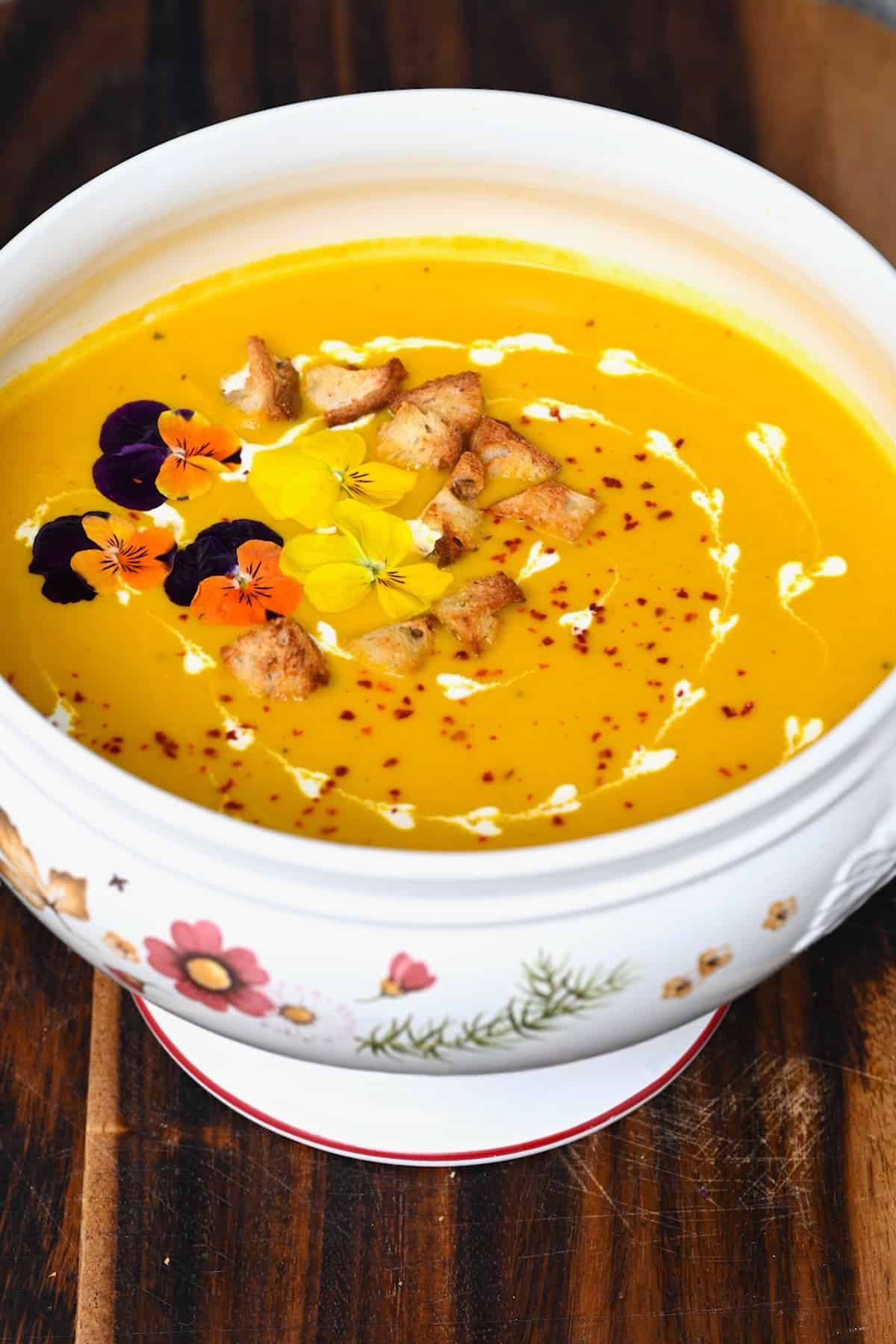 A serving bowl with carrot ginger soup topped with croutons and edible flowers