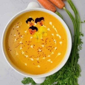 A serving bowl with carrot ginger soup topped with croutons and edible flowers