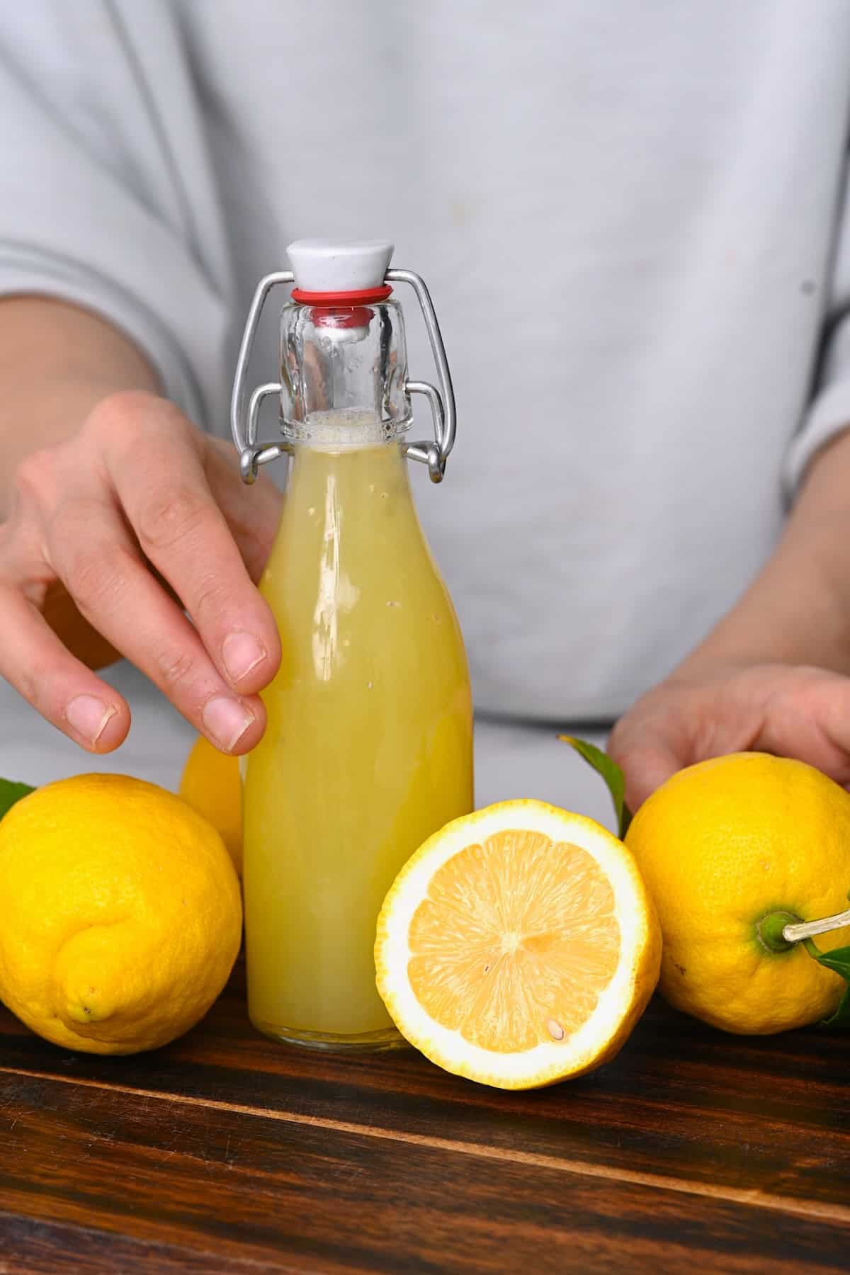 Hand holding a small bottle with lemon juice and thee lemons around it