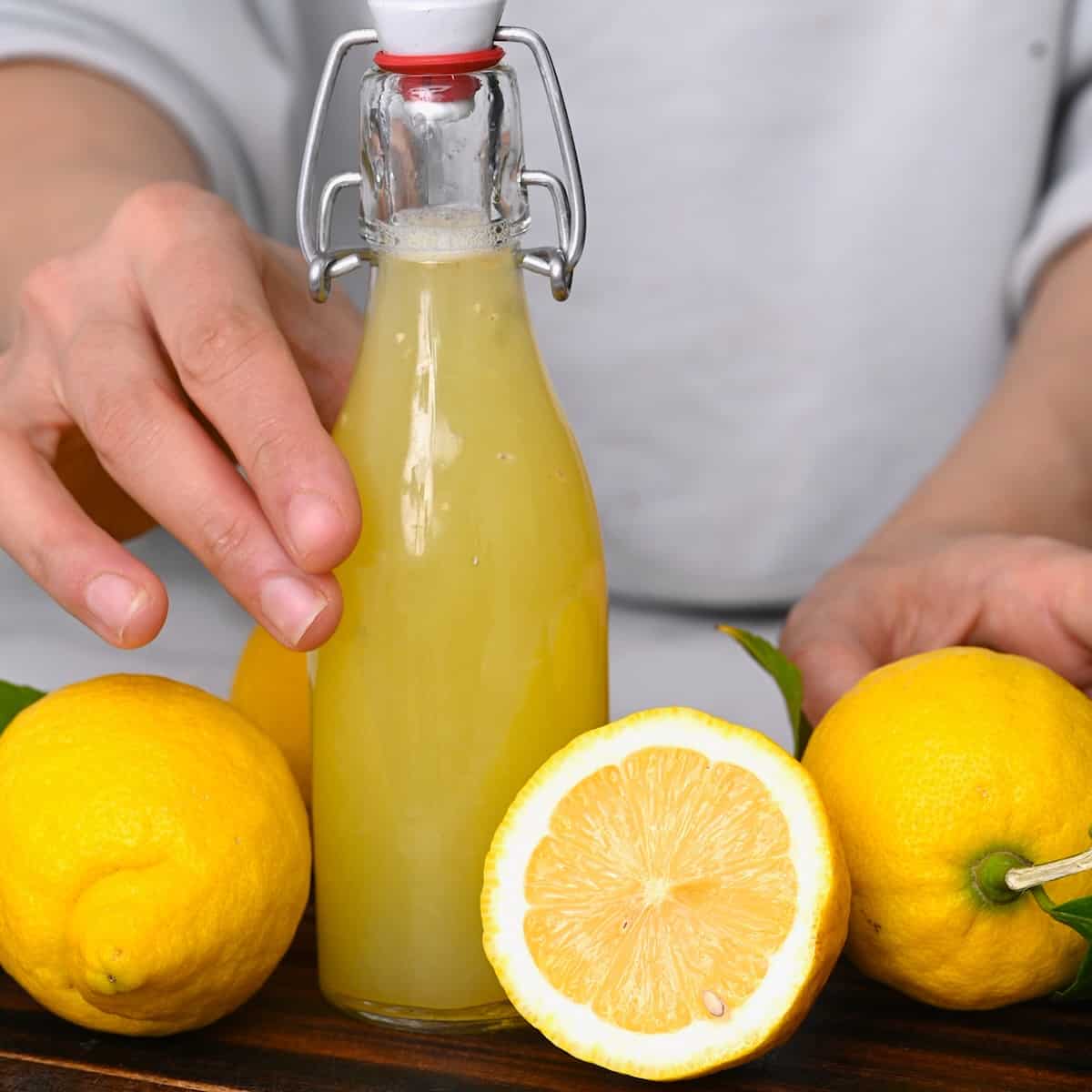 Hand holding a small bottle with lemon juice and thee lemons around it