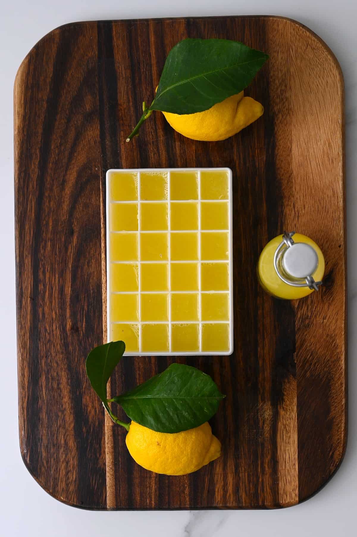 Two lemons a small bottle with lemon juice and an ice cube tray with lemon juice