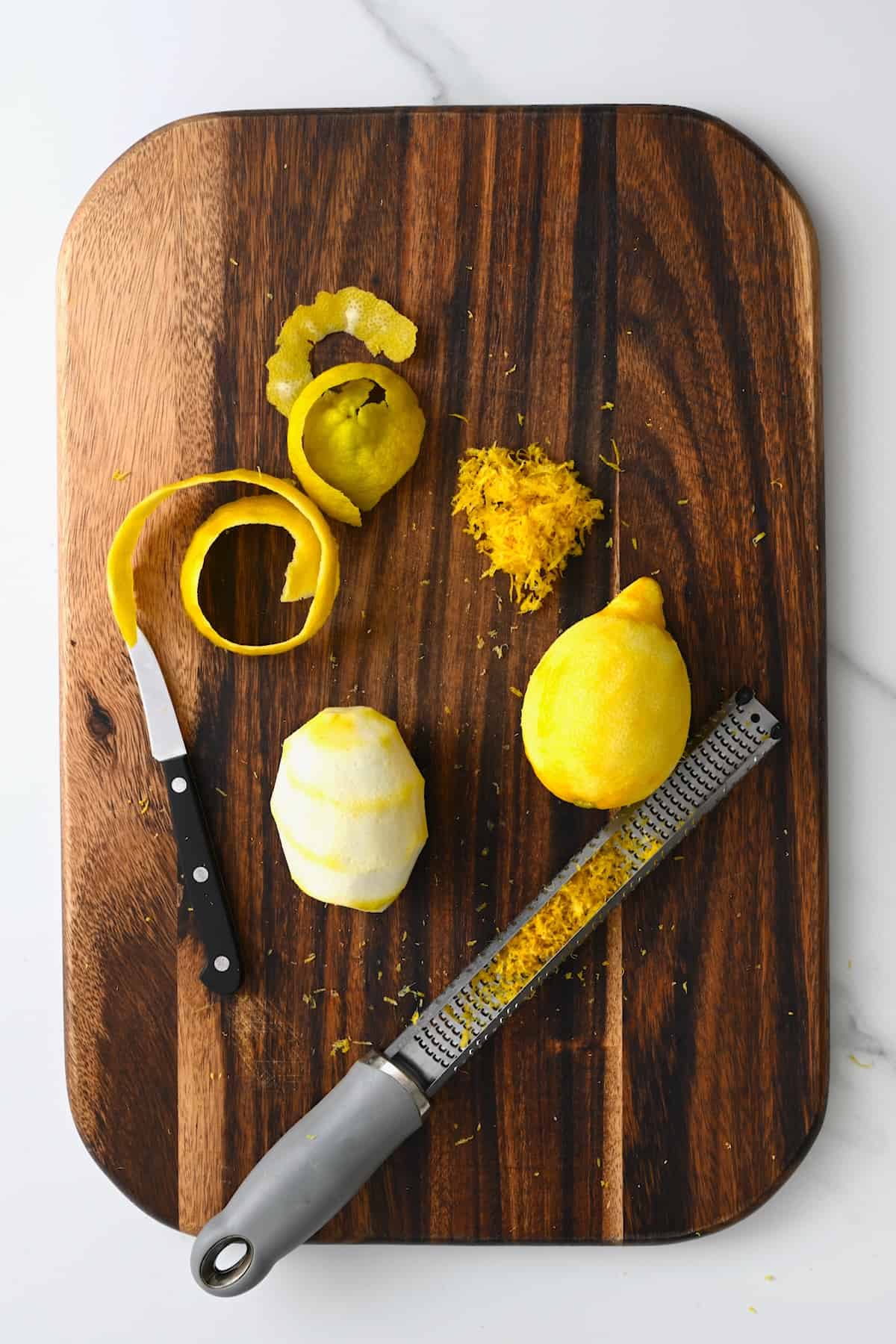 One peeled lemon with a knife and one zested lemon with a microplane