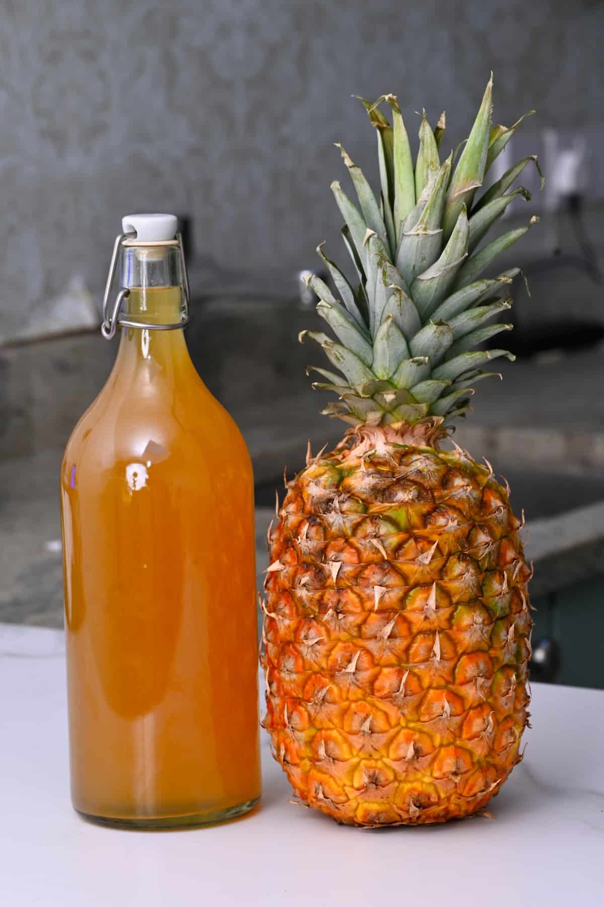 A bottle with tepache on a counter with a pineapple
