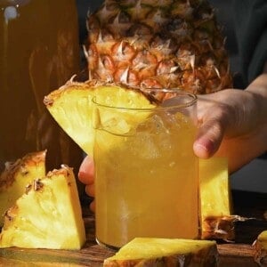 A glass with tepache and a slice of pineapple stuck on it