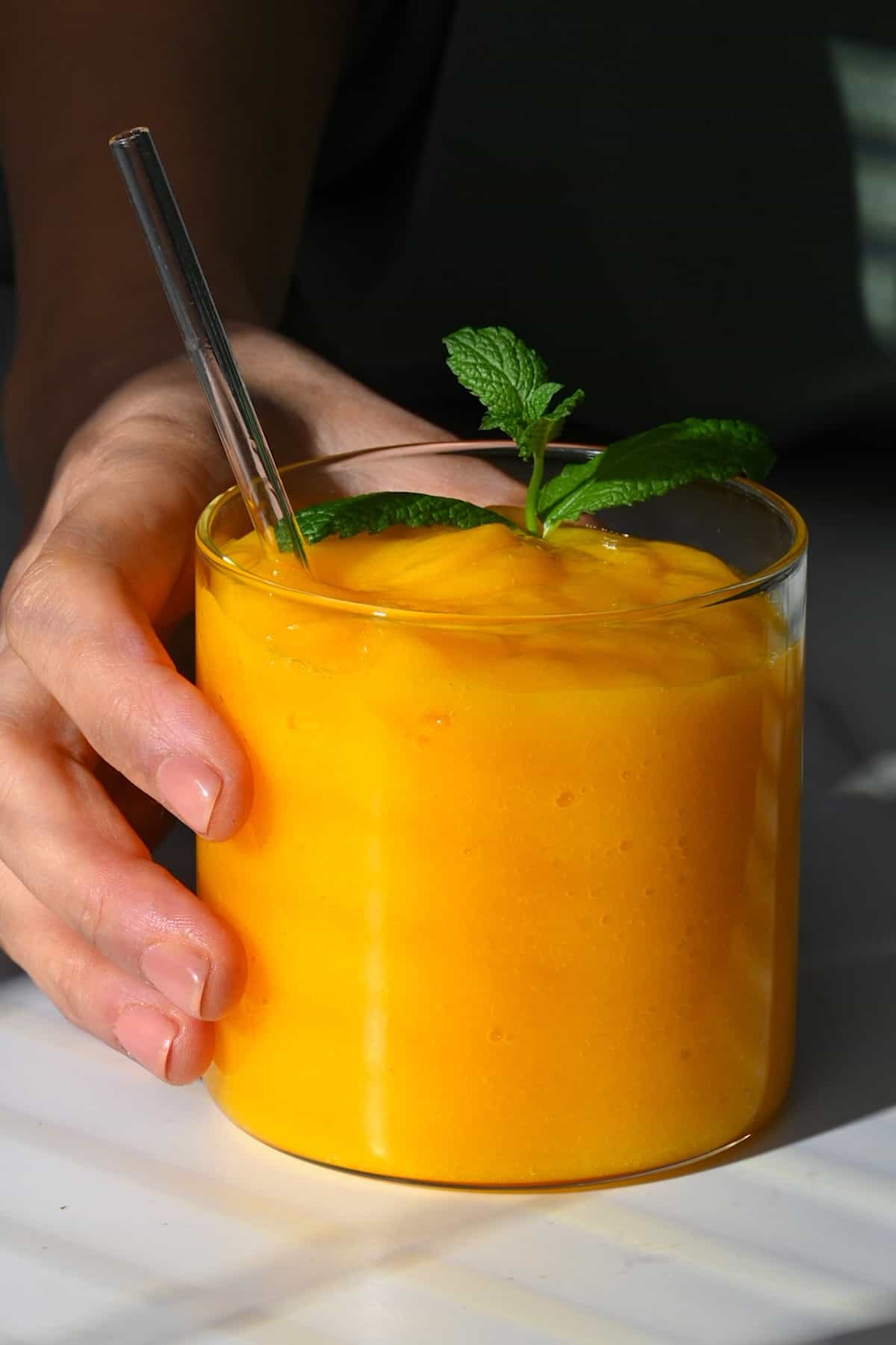 A glass with mango juice topped with mint leaves