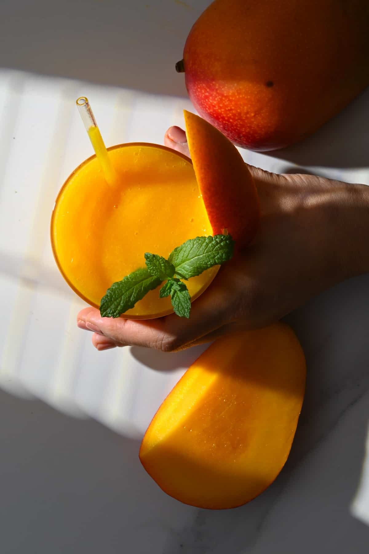 Hand holding a glass with mango juice on a flat surface