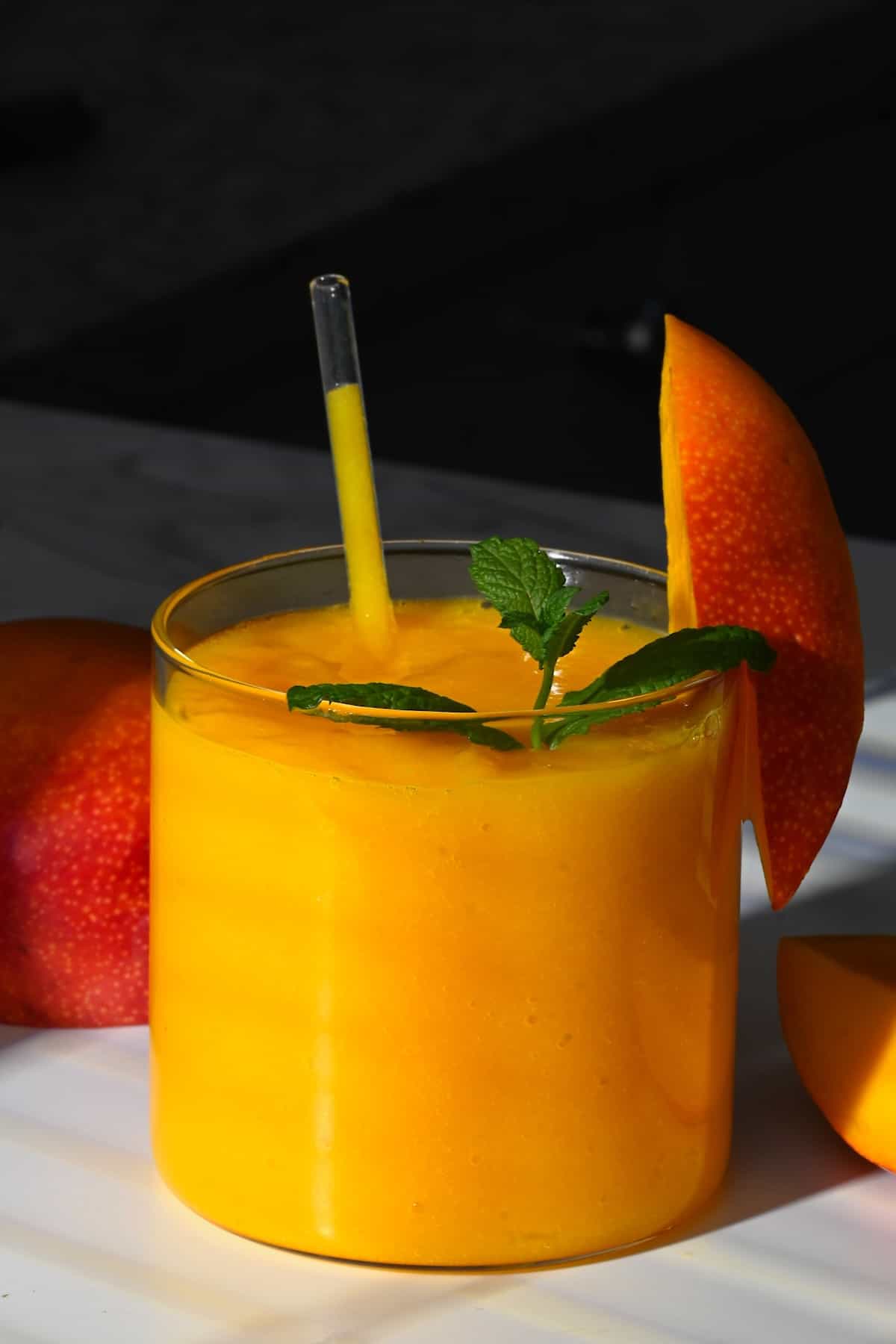A glass with mango juice topped with mint leaves and a mango piece