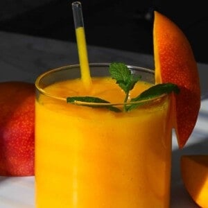 A glass with mango juice topped with mint leaves and a mango piece