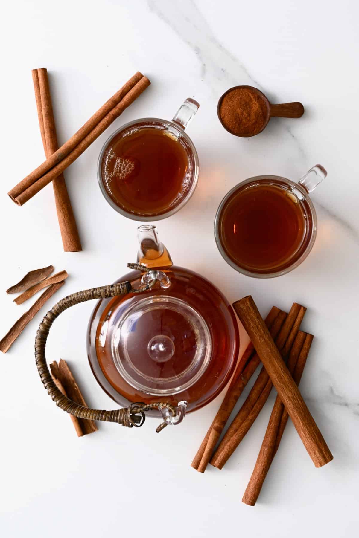 A tea pot and two cups with cinnamon tea and few cinnamon sticks around them