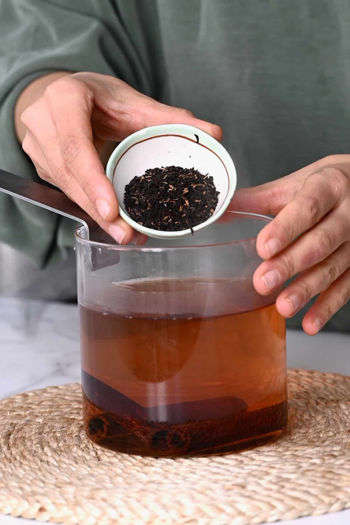 Adding loose black tea to a pot with cinnamon tea