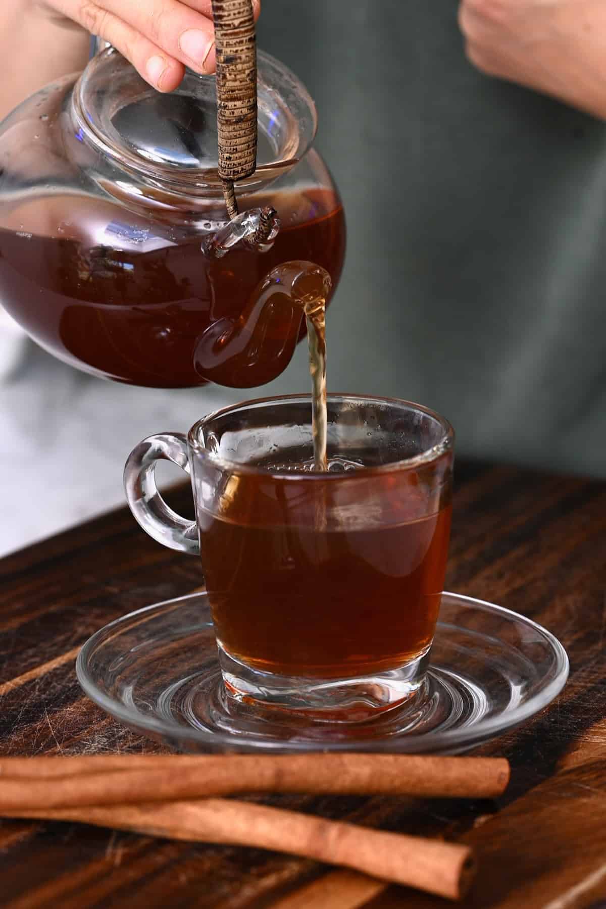 Pouring cinnamon tea from a tea pot into a glass cup