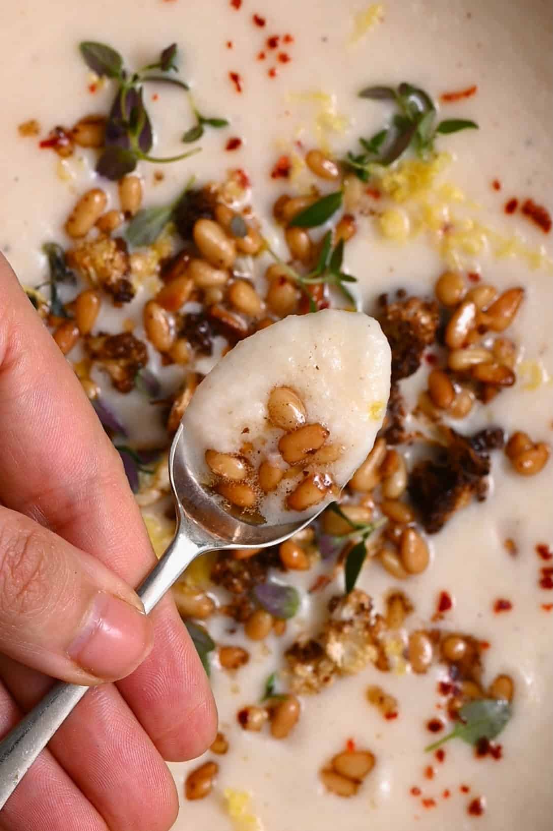 A spoonful of cauliflower soup topped with pine nuts