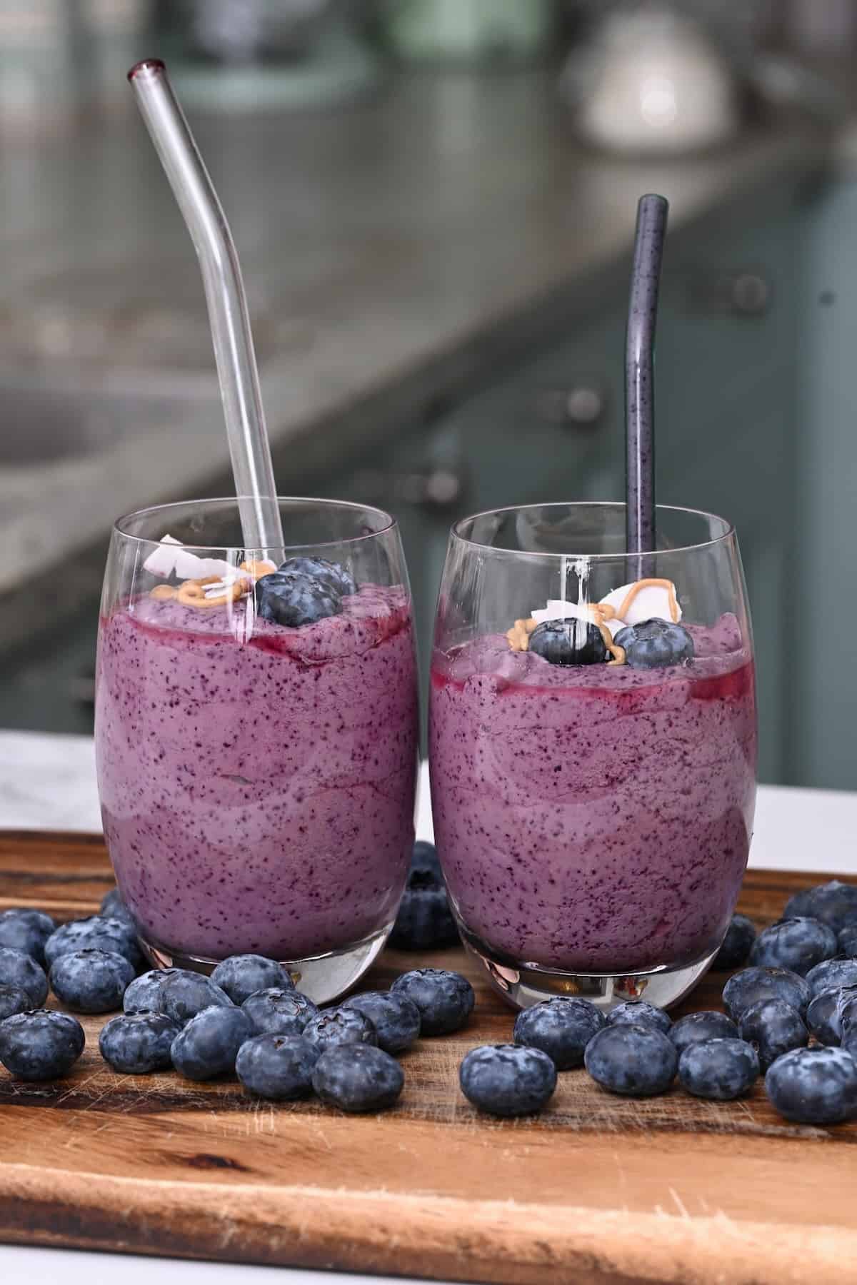 Two glasses with blueberry smoothie with straws and blueberries around them
