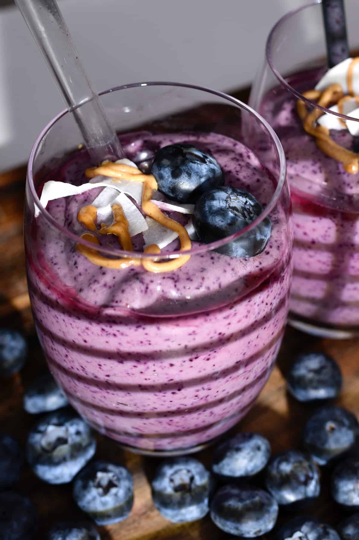 A glass with smoothie topped with blueberries and nut butter