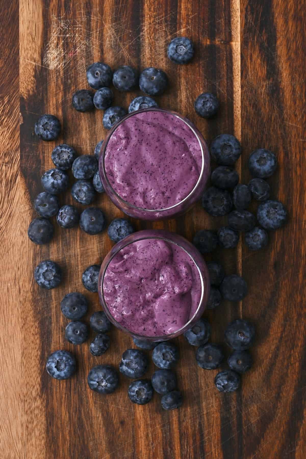 Top view of two glasses with purple smoothie and blueberries around them