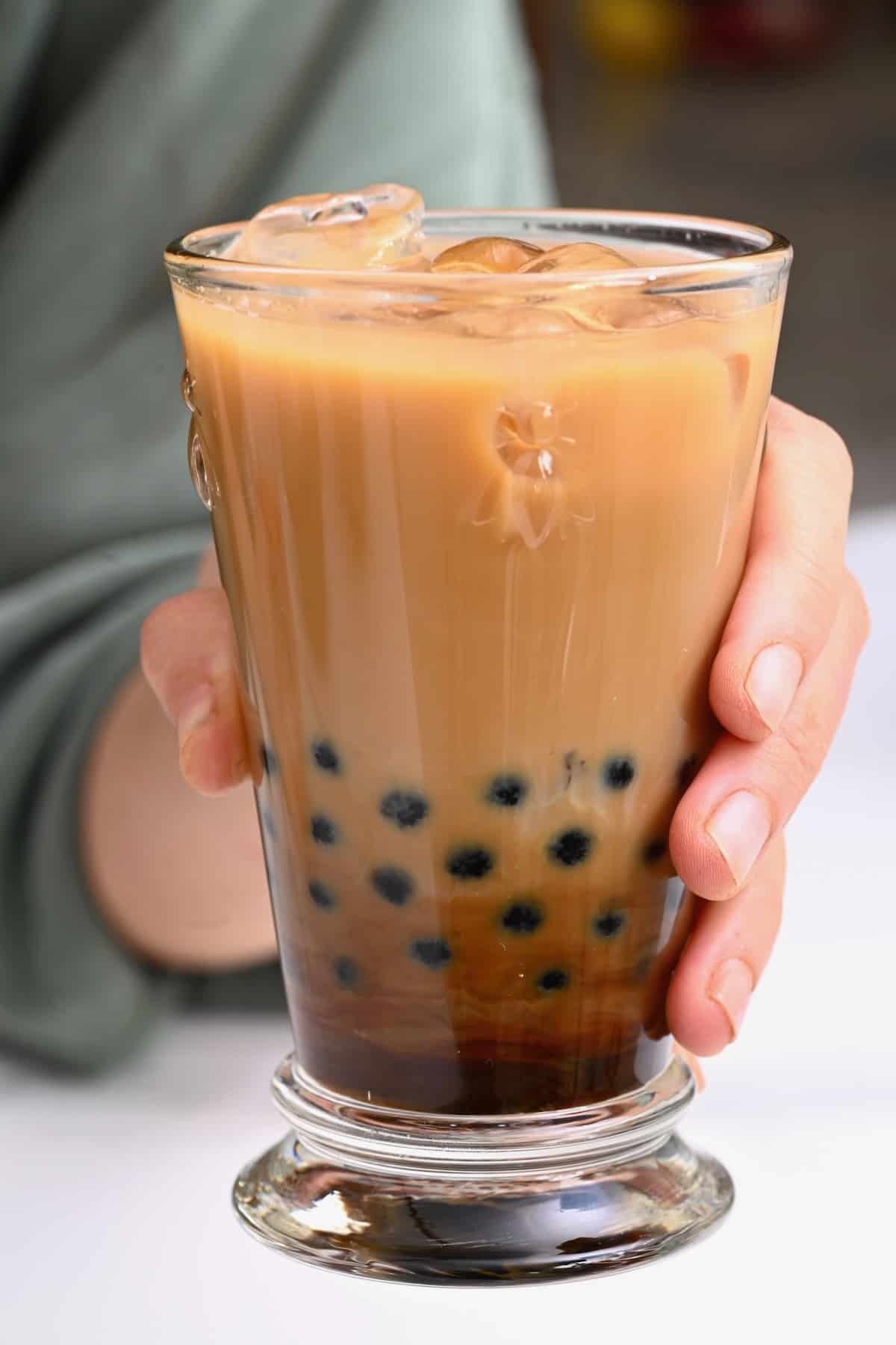A hand holding a glass with bubble milk tea