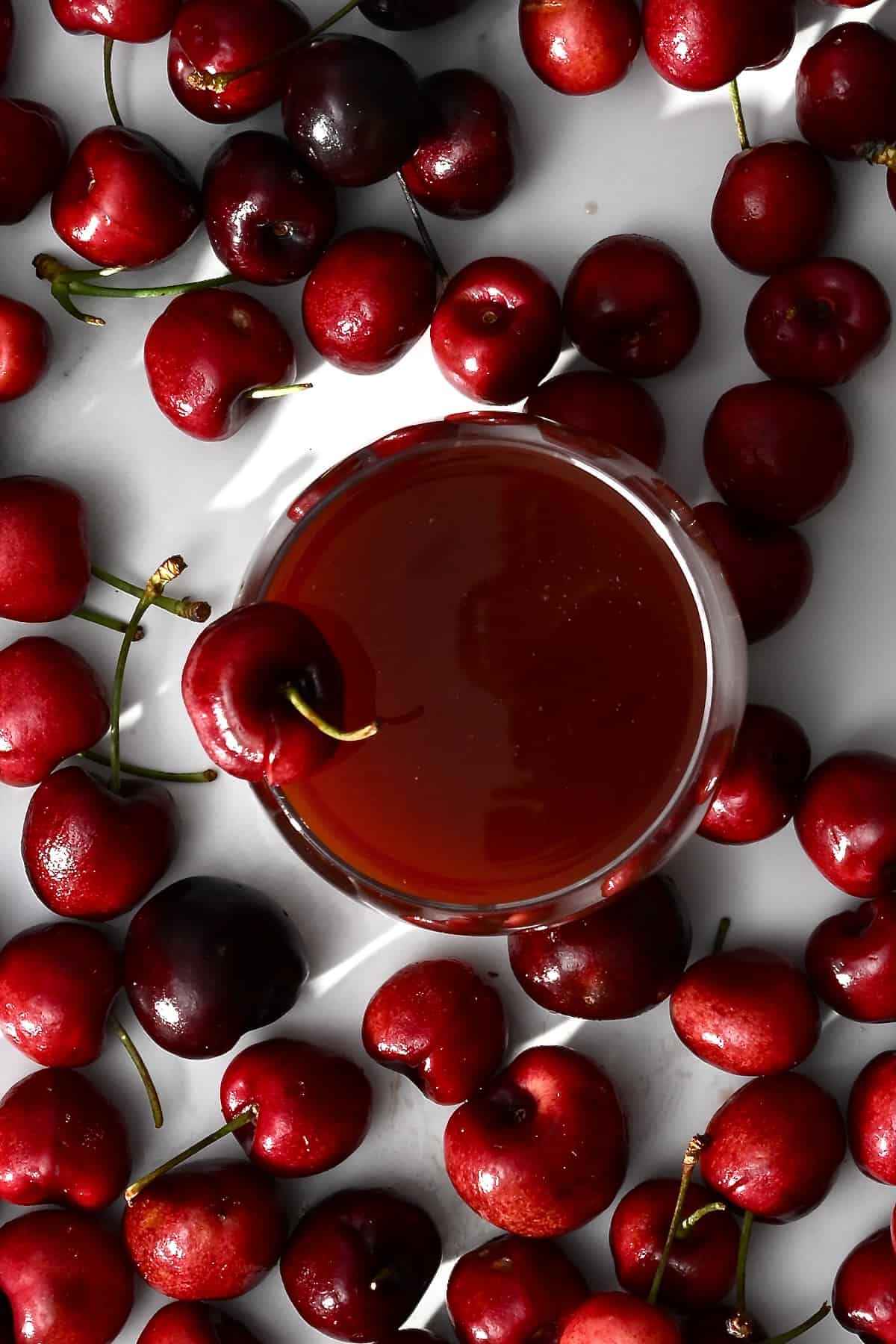 A glass of cherry juice and lots of cherries around it