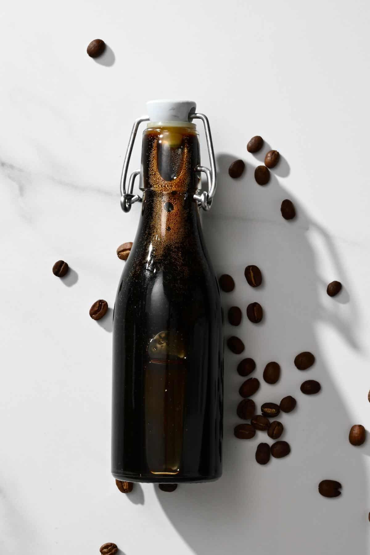 Homemade coffee syrup in a bottle with few coffee beans around it
