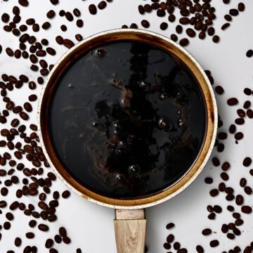 Homemade coffee syrup in a pot with coffee beans around it