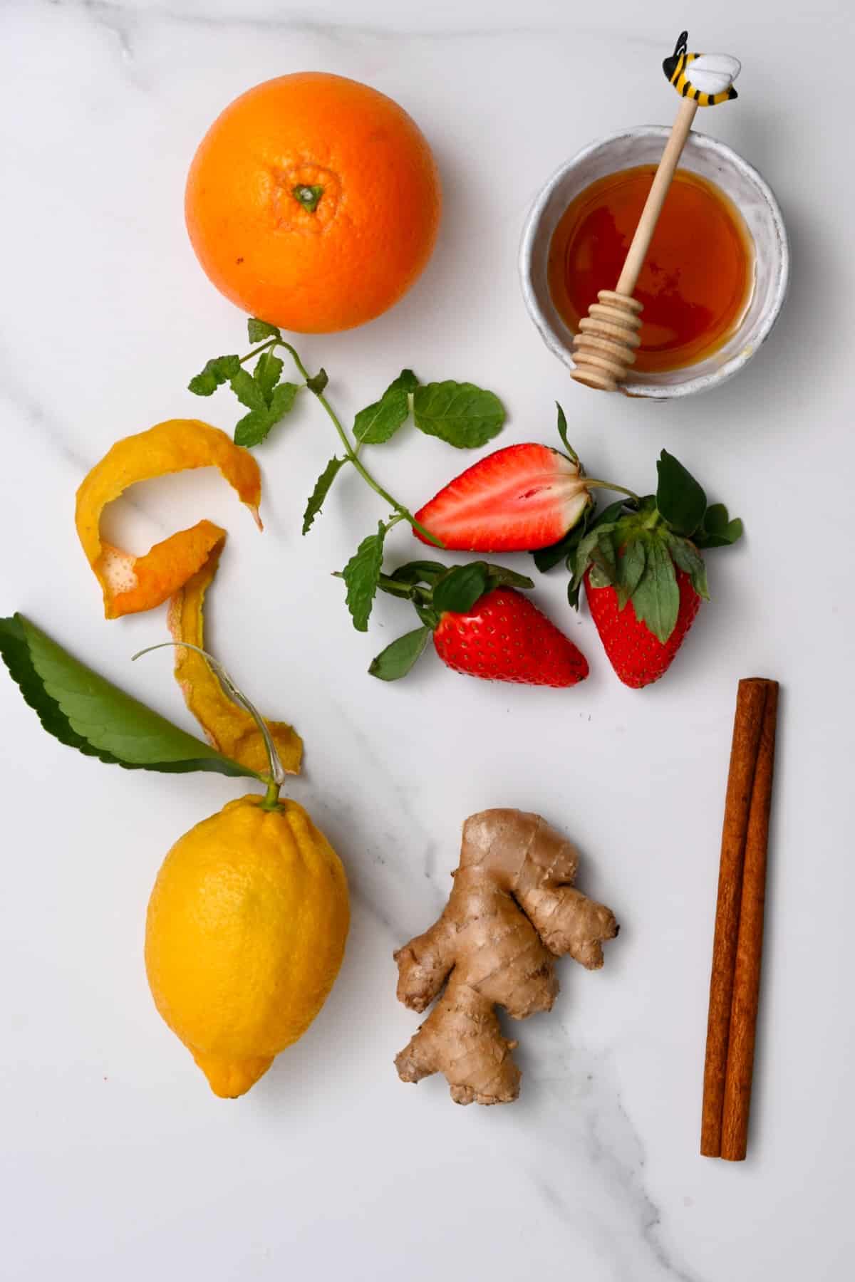 Orange, lemon, strawberries, honey, ginger and cinnamon on a flat surface