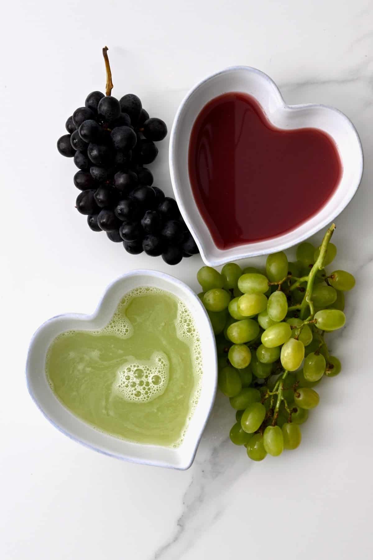 Black grapes, a bowl of red grape juice, a bowl of green grape juice, and green grapes