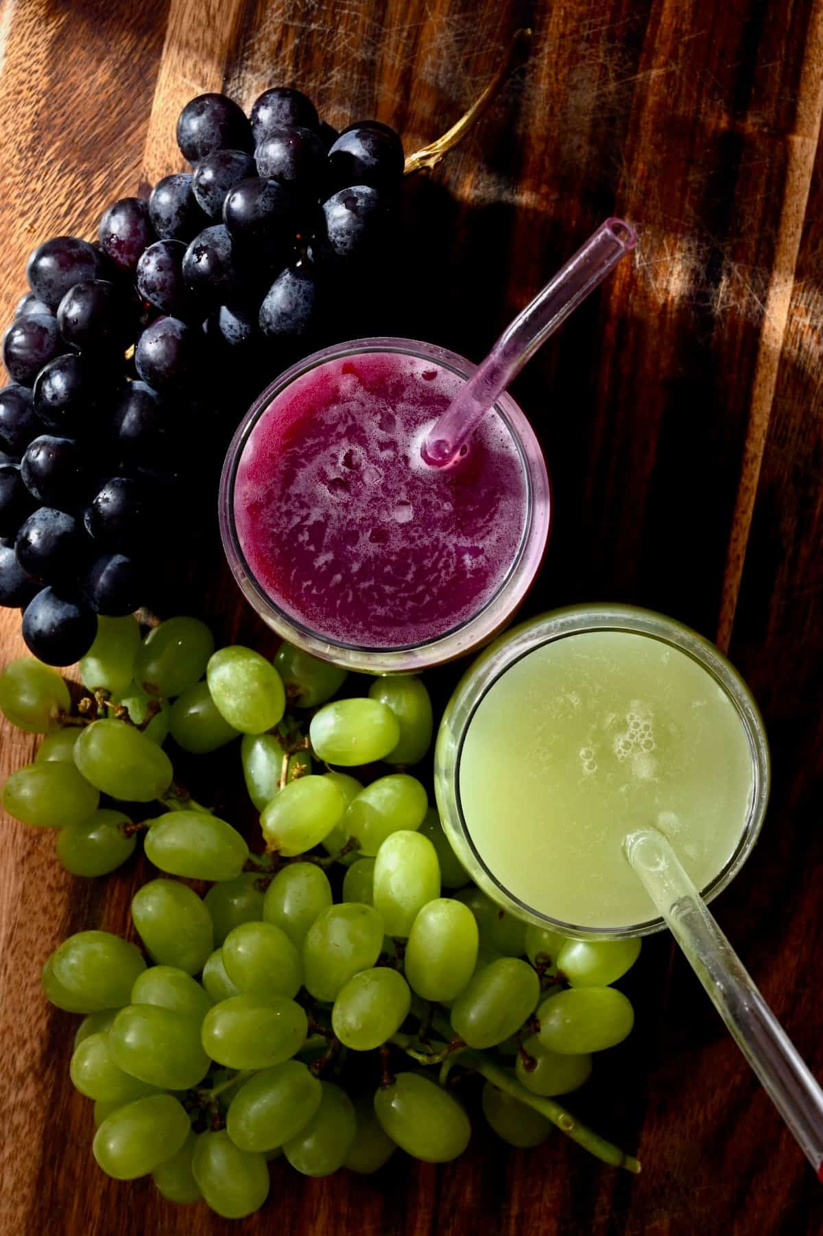 Two grasses with red and green grape juice and grapes around them