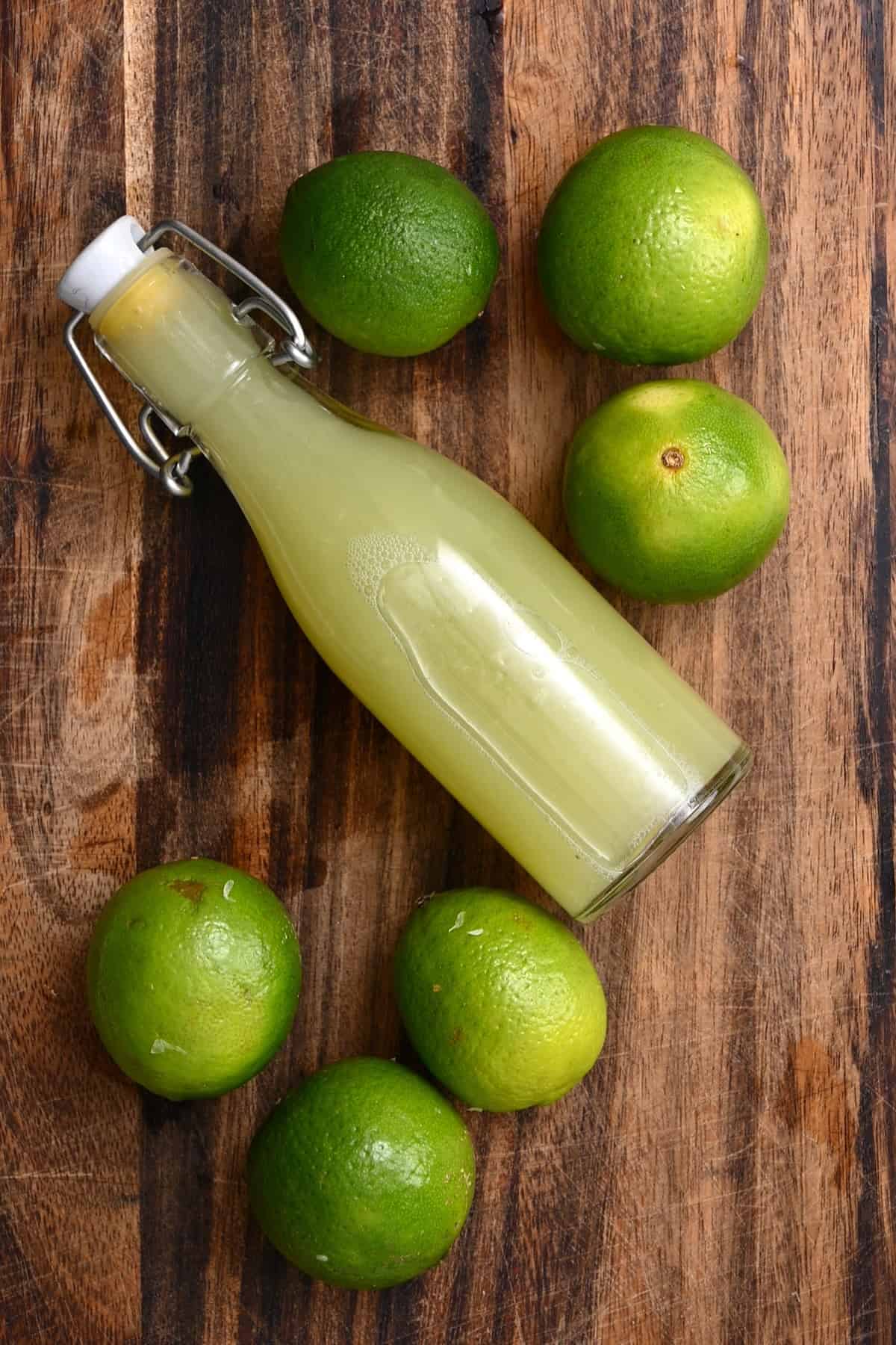 A small bottle with lime juice and limes on a chopping board