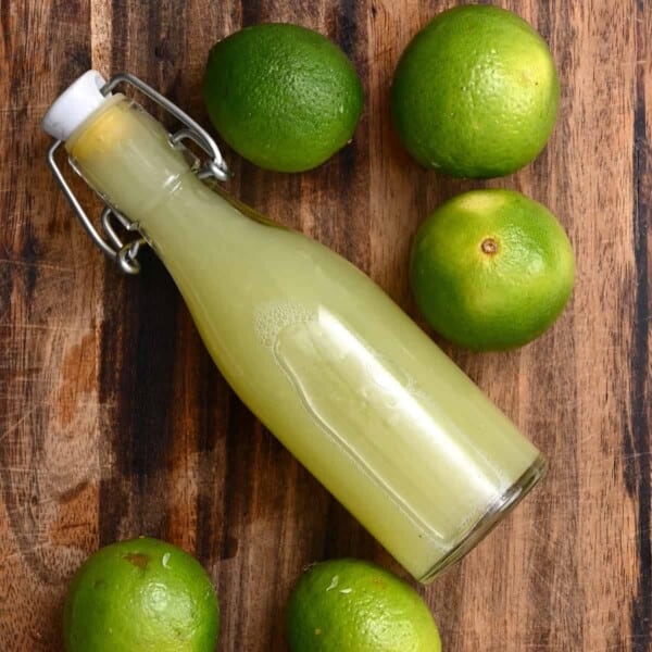 A small bottle with lime juice and limes on a chopping board