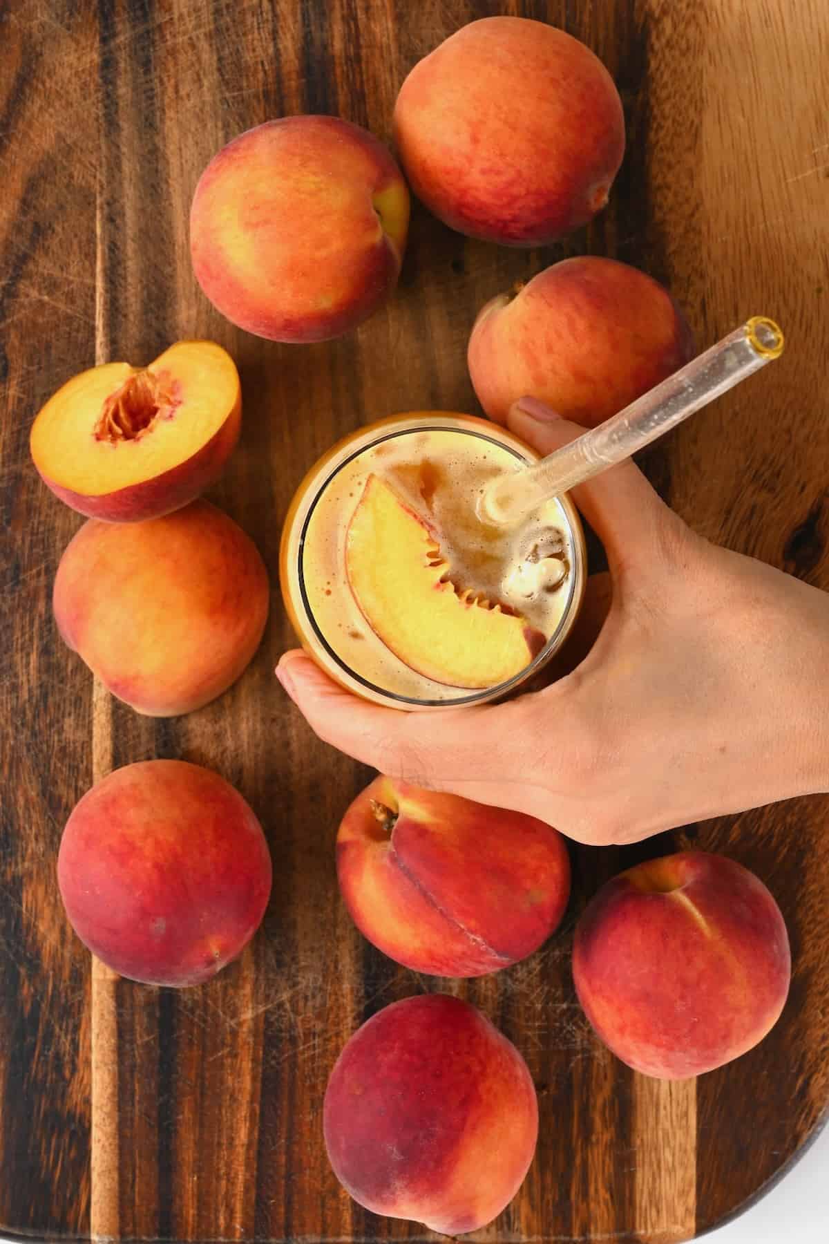 A glass with peach juice and peaches around it