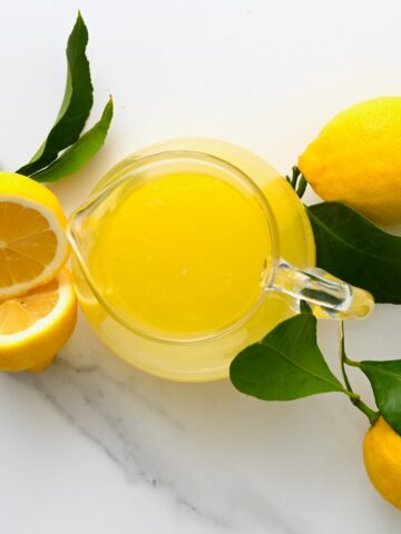 A pitcher with lemon juice and three lemons around it