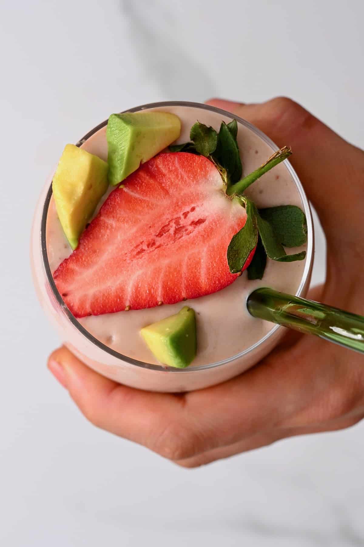 Top view of a glass with smoothie topped with strawberry and avocado