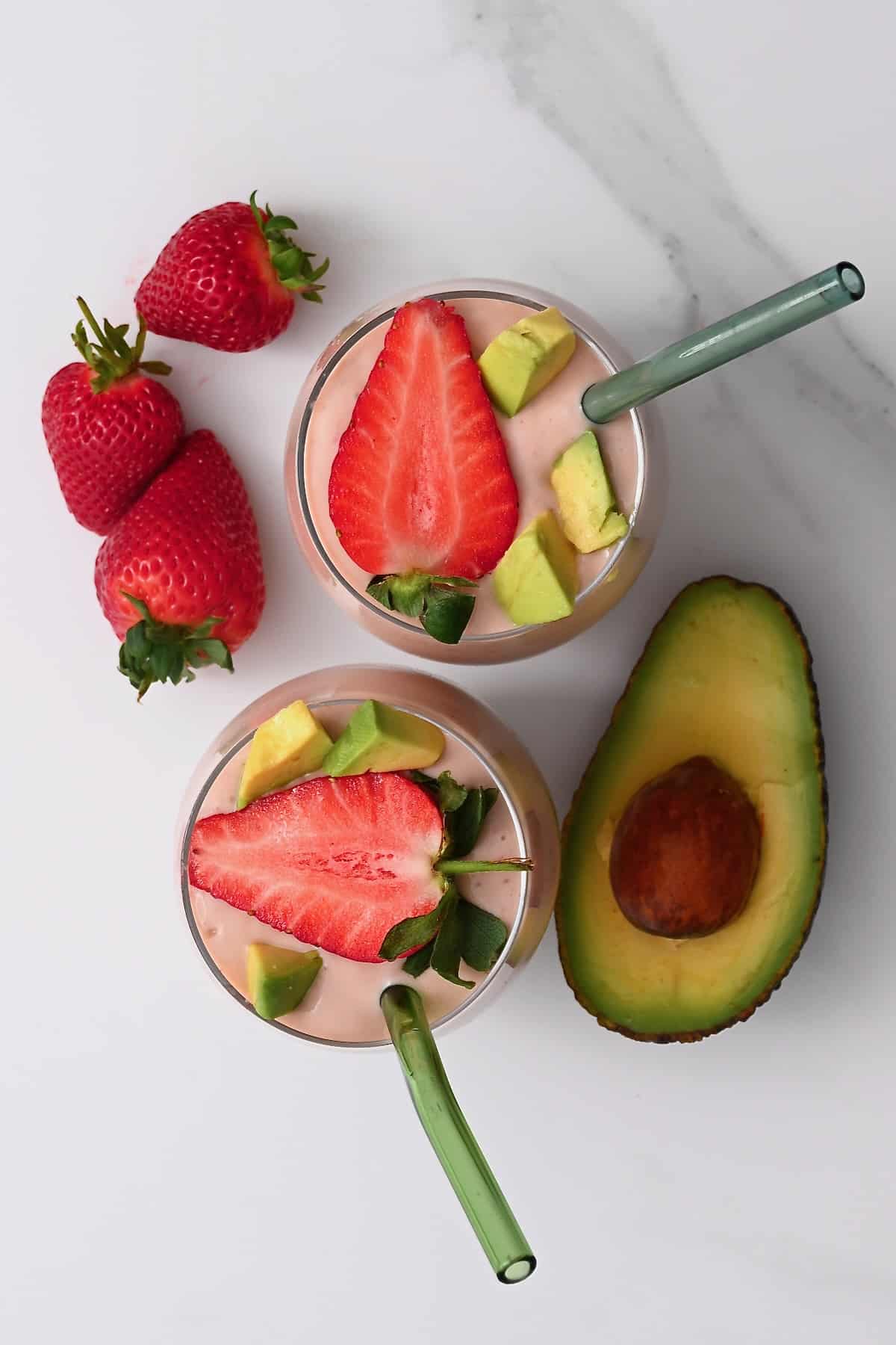 Top view of two glasses with smoothie topped with strawberry and avocado