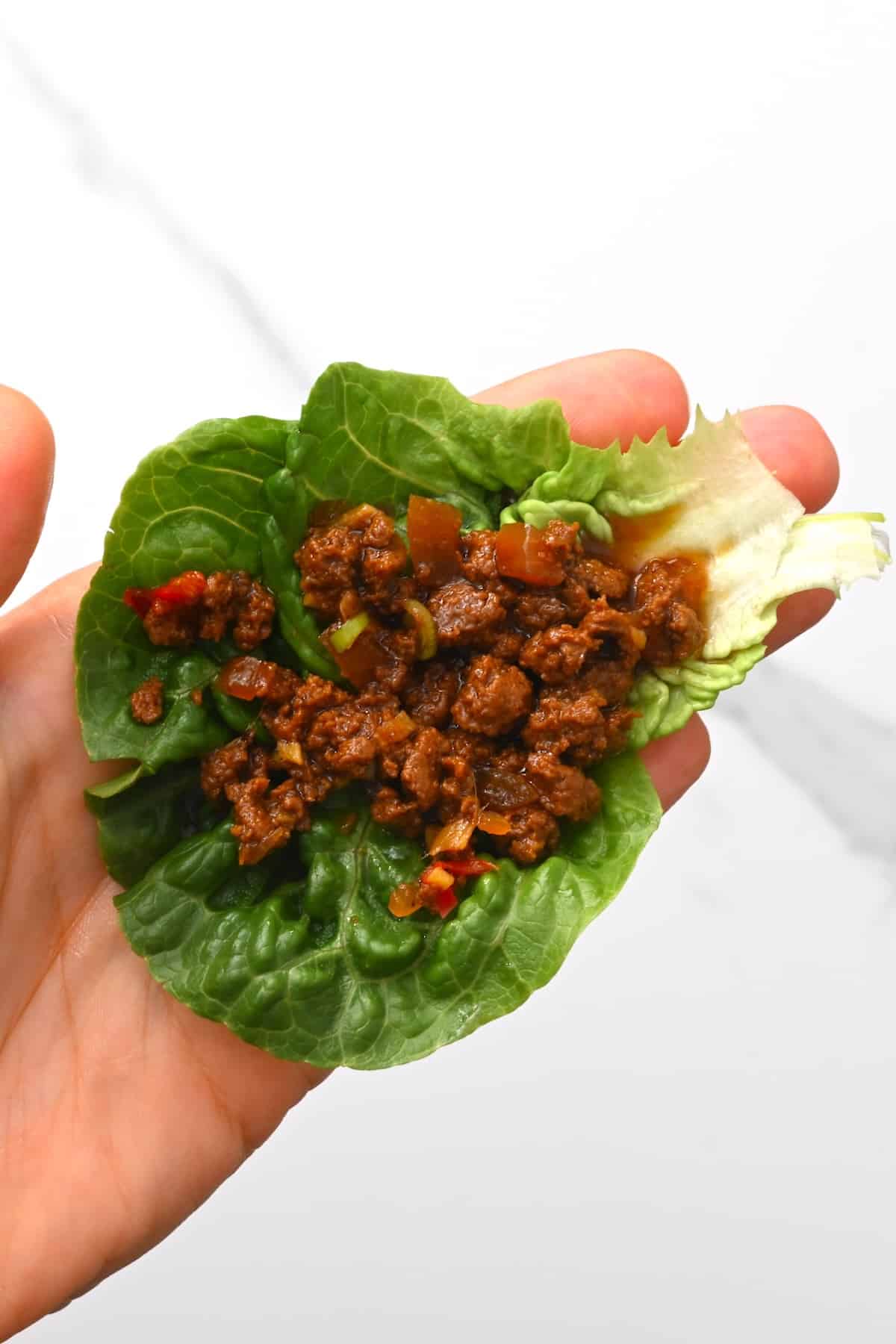Hand holding a lettuce wrap with meat filling