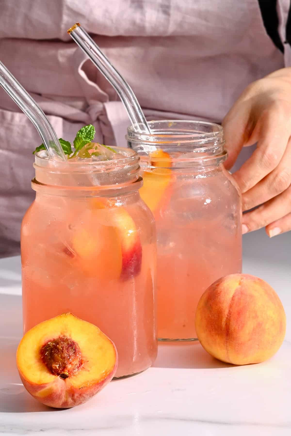 Two glasses with peach lemonade and two peaches in front of them