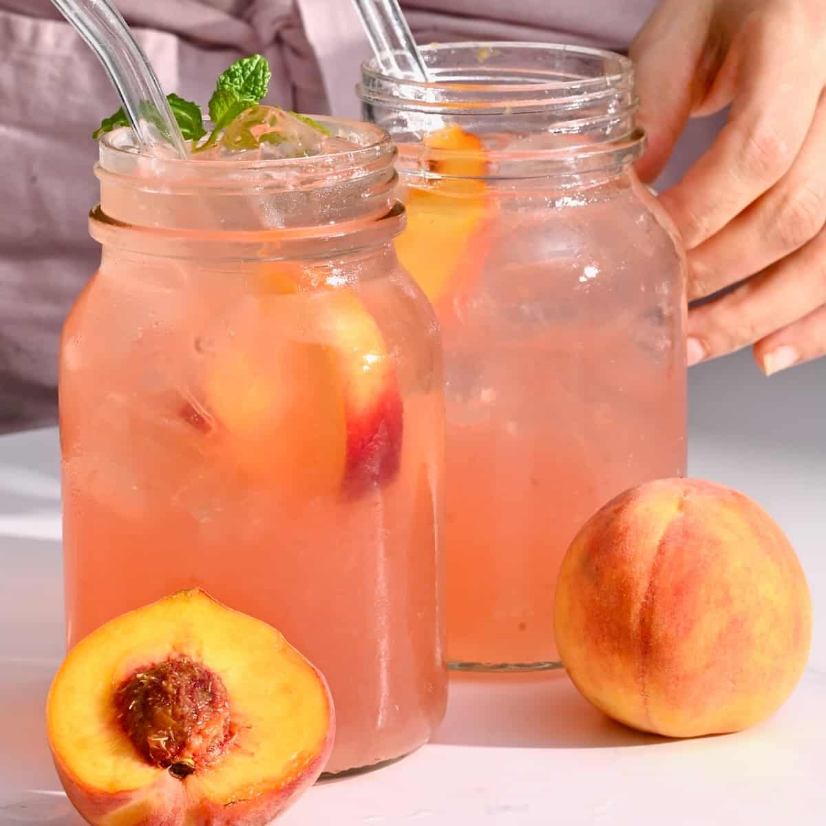 Two glasses with peach lemonade and two peaches in front of them