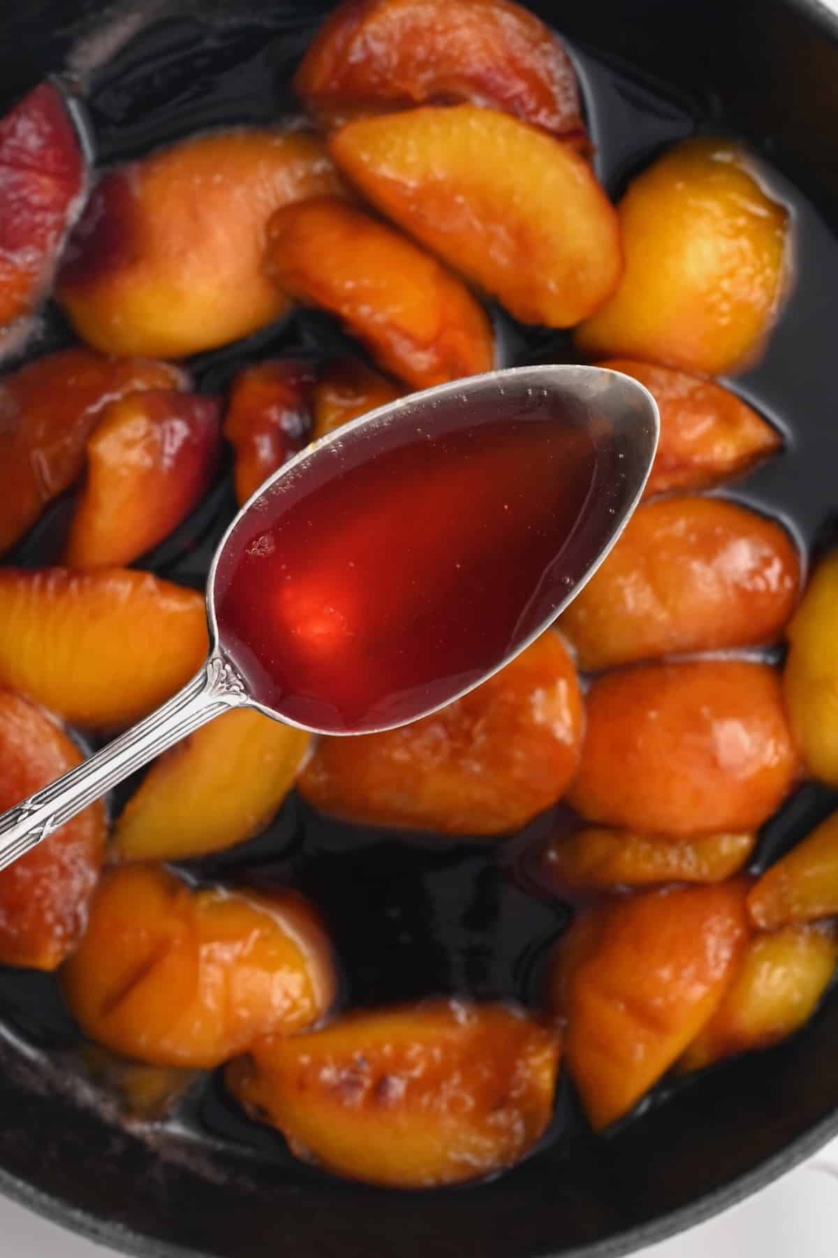 A spoonful of peach syrup over a pan with peaches