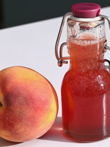 A small bottle with peach syrup and a peach next to it
