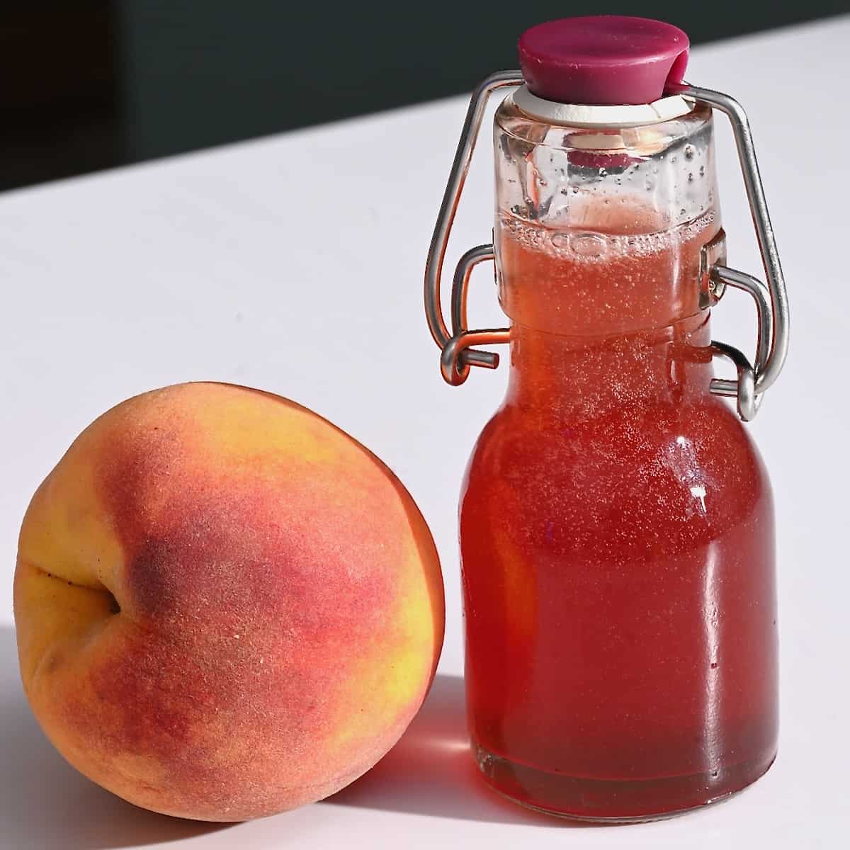 A small bottle with peach syrup and a peach next to it