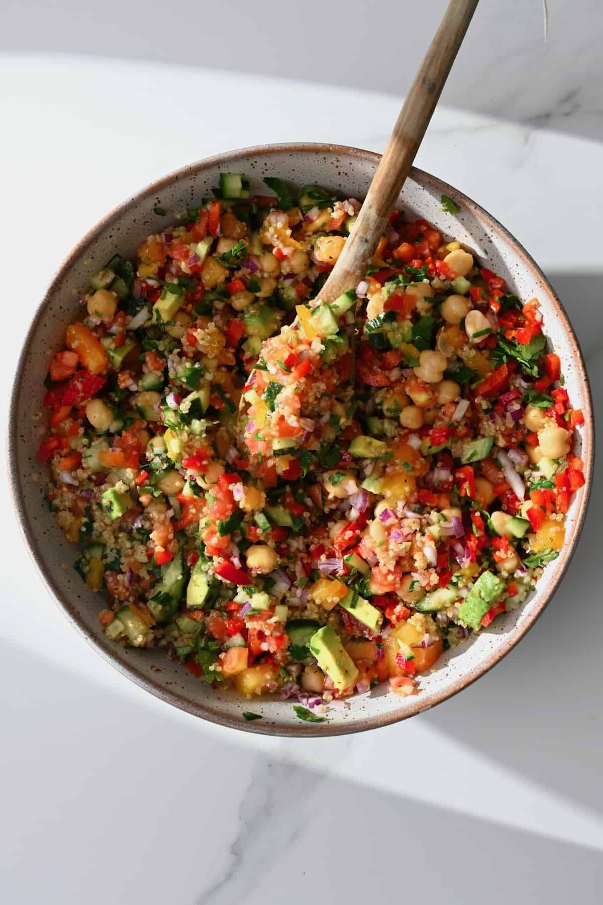 A bowl with quinoa salad with veggies and a wooden spoon