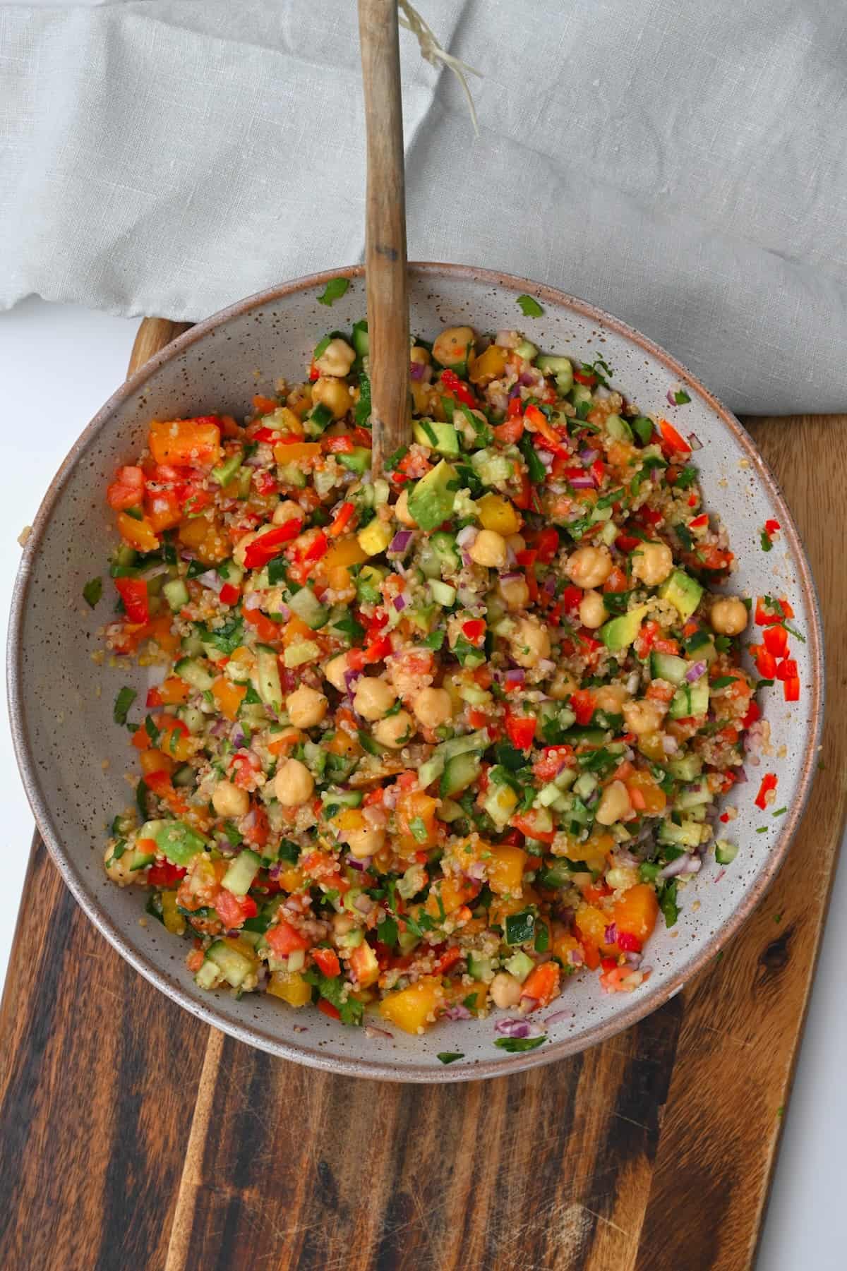 A wooden spoon in a bowl with quinoa chickpea salad