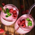 Two glasses of raspberry smoothie topped with raspberries and mint