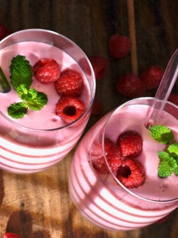 Two glasses of raspberry smoothie topped with raspberries and mint